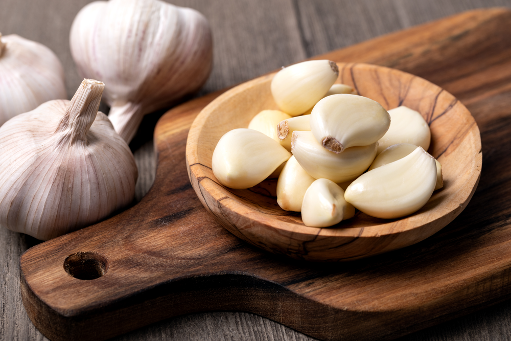 Cloves of garlic, peeled and unpeeled, on a wooden board.